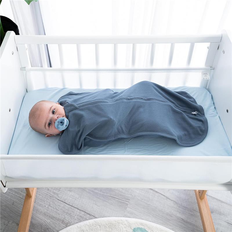 Baby swaddled in a blue Comfy Cubs blanket with a pacifier, lying in a crib on a light blue mattress.