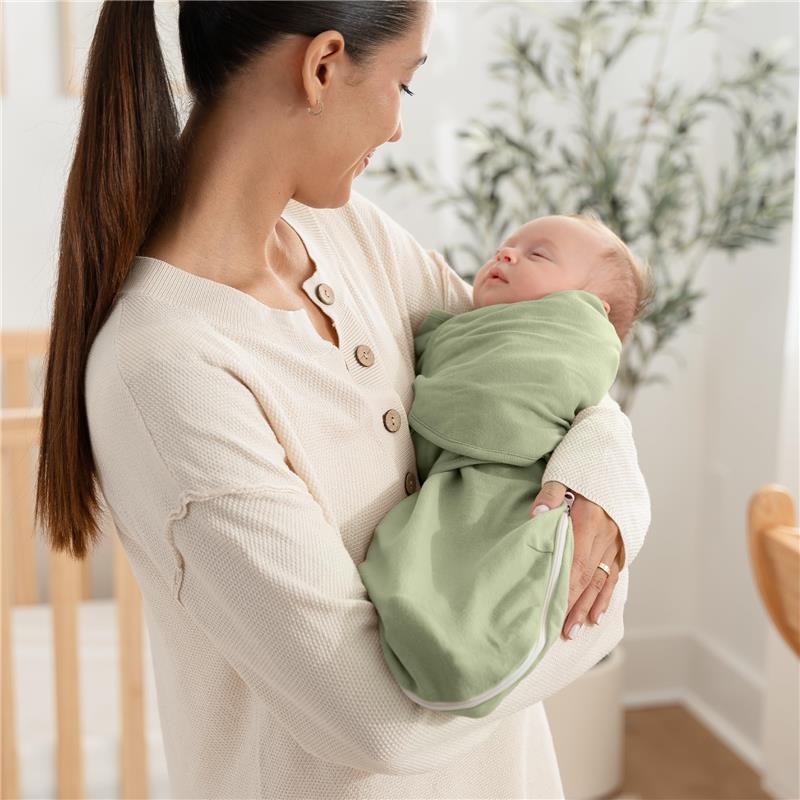 A mother holds an infant swaddled in a green Comfy Cubs Easy Swaddle Blanket with zipper closure, smiling in a cozy room.
