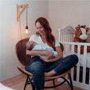 Woman sitting in a chair, gently holding a swaddled baby in blue striped muslin blanket, with a nursery setting in the background.