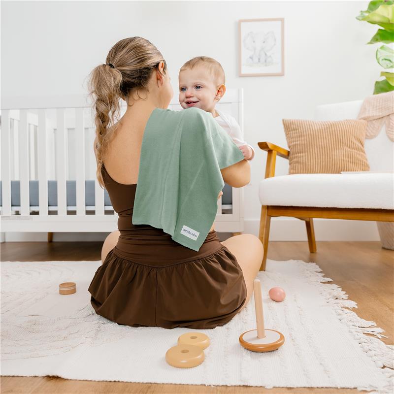 Mom holding a smiling baby, using a green burp cloth, in a warmly decorated nursery with toys and a crib.
