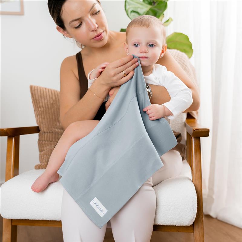 A woman gently wipes the face of a baby with a light blue burp cloth, showcasing the Comfy Cubs brand.