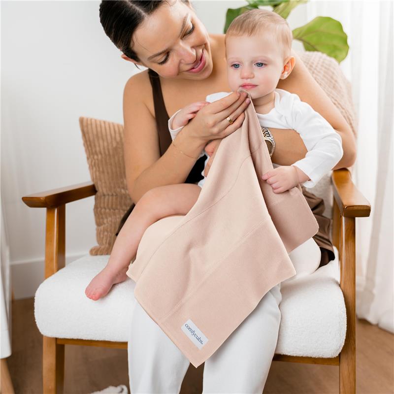 A woman holds a baby on her lap, using a soft, absorbent beige burp cloth from the Comfy Cubs set.