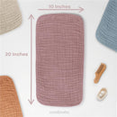 Multi-colored muslin burp cloths in pink, beige, and blue, displaying dimensions of 10 x 20 inches, with a wooden comb and baby products.