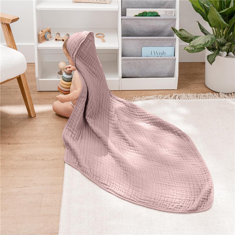 Hooded mauve baby towel draped over a sitting baby playing with colorful stacking toys on a light rug.