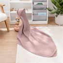 Hooded mauve baby towel draped over a sitting baby playing with colorful stacking toys on a light rug.