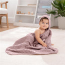 Hooded mauve towel wrapped around a baby sitting on the floor, smiling with playful expression.