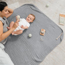 Muslin baby blanket in Heather Blue with a mother and baby playing; includes toys like a rattle and a wooden camera.