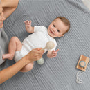 Muslin baby blanket in heather blue with a smiling baby in a white onesie holding a wooden rattle, surrounded by toys.
