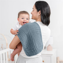 Muslin burp cloth draped over a woman’s shoulder, holding a smiling baby; soft, textured fabric in a muted blue.