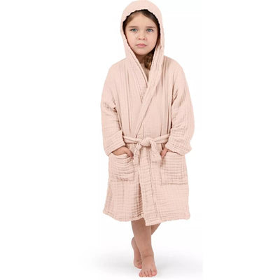 Muslin kids bathrobe in blush color, featuring a hood and pockets, worn by a girl standing barefoot.