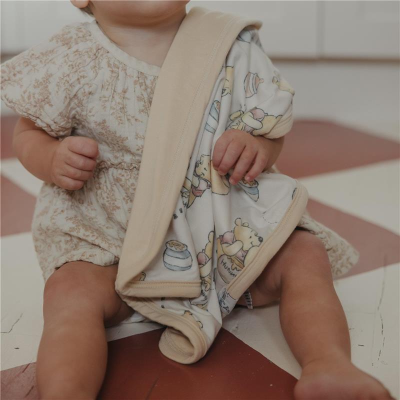 Infant sitting on the floor holding a 3-layer knit blanket featuring a whimsical bear pattern, part of the Copper Pearl Hunny set.