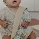 Baby wearing a floral dress holds a soft blanket featuring Winnie the Pooh illustrations in light colors.