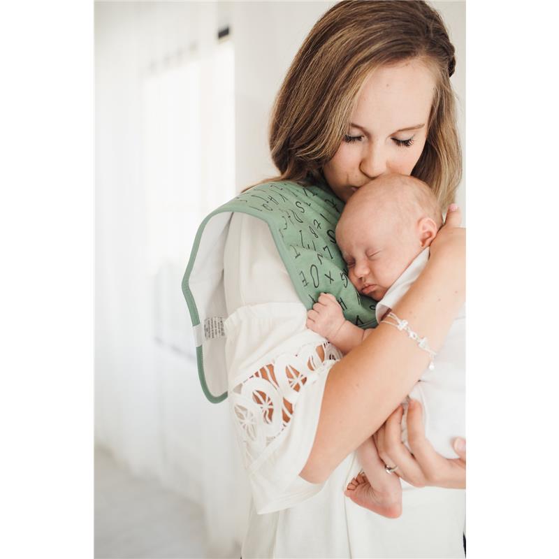 A mother gently kisses her sleeping baby, who is cradled in her arm while wearing a green burp cloth with patterns.