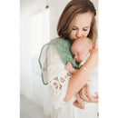 A mother gently kisses her sleeping baby, who is cradled in her arm while wearing a green burp cloth with patterns.