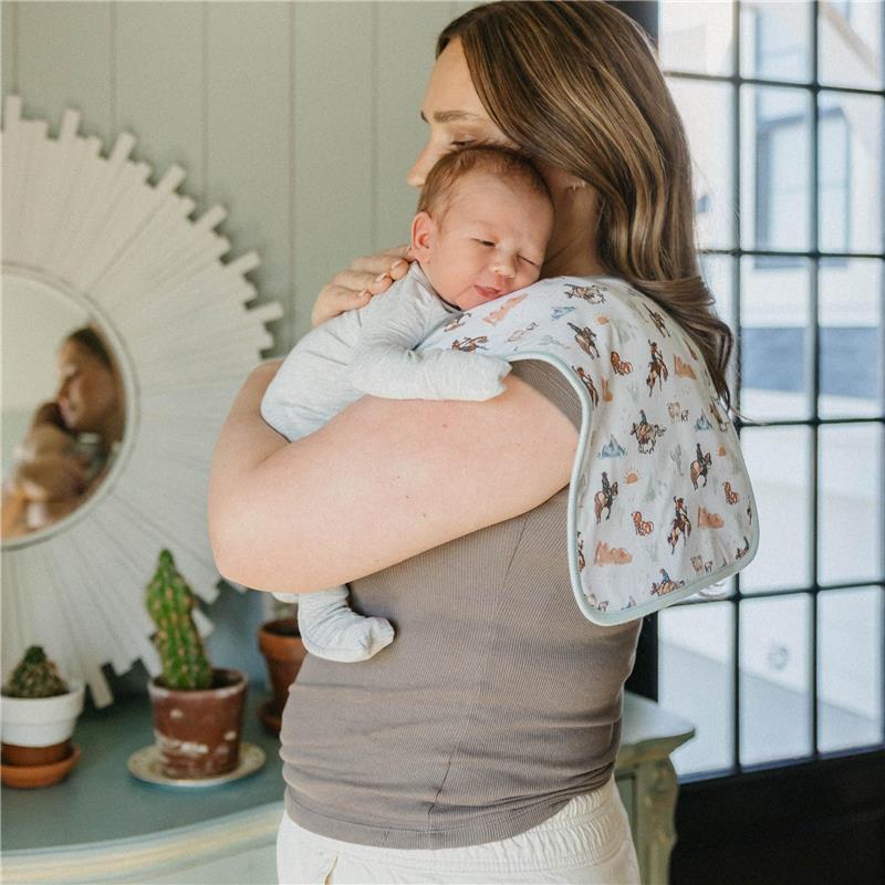 Mom holds a baby in a light gray outfit, using a colorful burp cloth with animal prints draped over her shoulder.