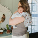 Mom holds a baby in a light gray outfit, using a colorful burp cloth with animal prints draped over her shoulder.