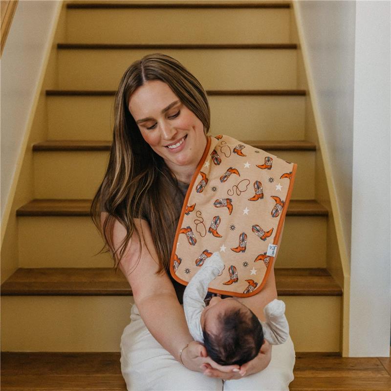 A smiling woman sitting on stairs holds a baby wearing a burp cloth featuring colorful designs.
