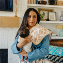 Woman holding a baby while wearing a Copper Pearl burp cloth with a goosie design, in a cozy home setting.