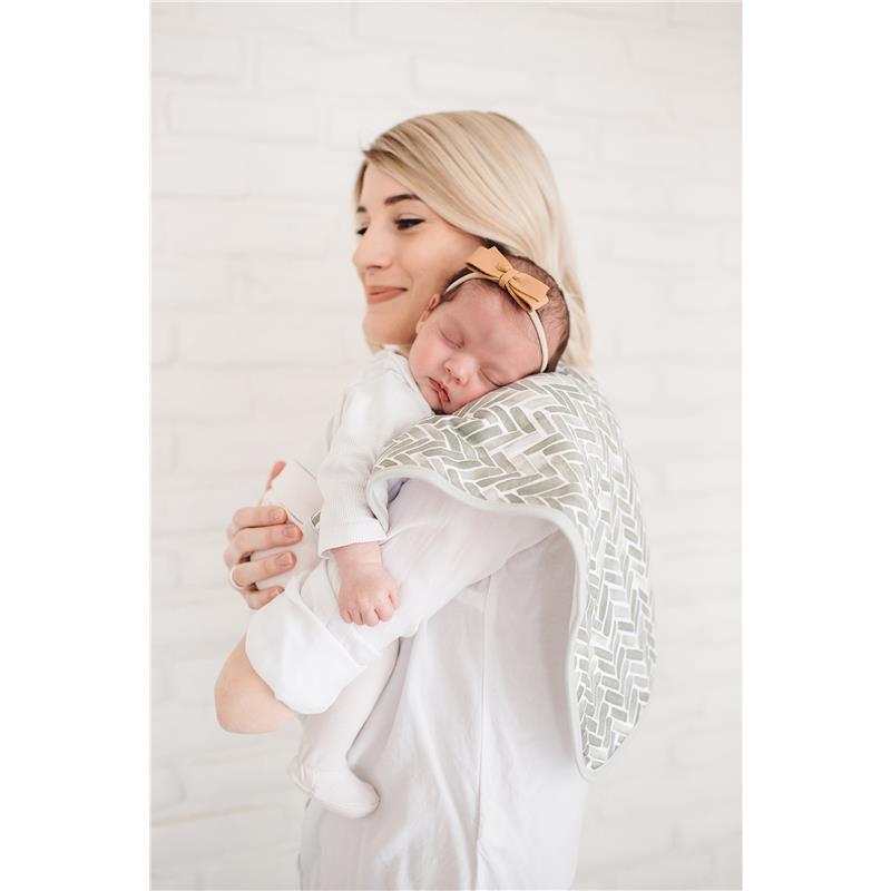 A woman holds a sleeping baby draped with a Copper Pearl burp cloth featuring a green herringbone pattern.