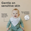 Baby wearing a white bandana bib smiles at the camera, with text highlighting its gentle, breathable cotton and ultra-soft fleece features.