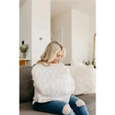 A woman seated on a couch uses a Bliss Canopy baby car seat cover by Copper Pearl, depicted in a modern living space.