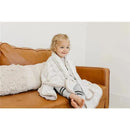 Toddler wrapped in a Bliss Knit 3 Layer Stretchy Quilt Blanket sitting on a brown couch, smiling happily.