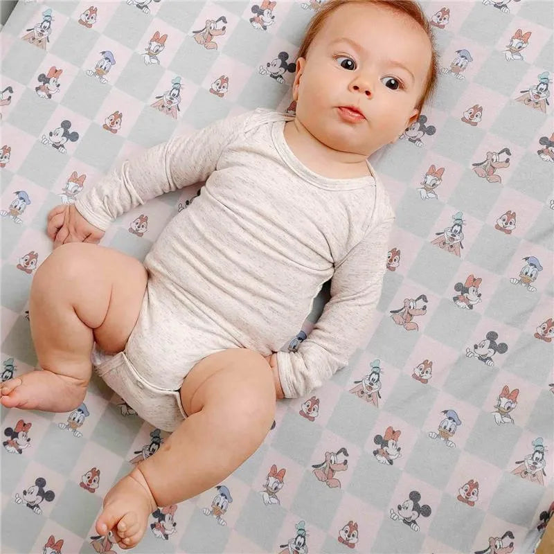 Infant lying on a Copper Pearl Disney Mickey Mouse & Friends crib sheet featuring cartoon characters in pastel colors.