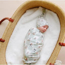 Mickey Mouse & Friends Top Knot Hat on a sleeping baby, swaddled in matching fabric, resting in a woven bassinet.