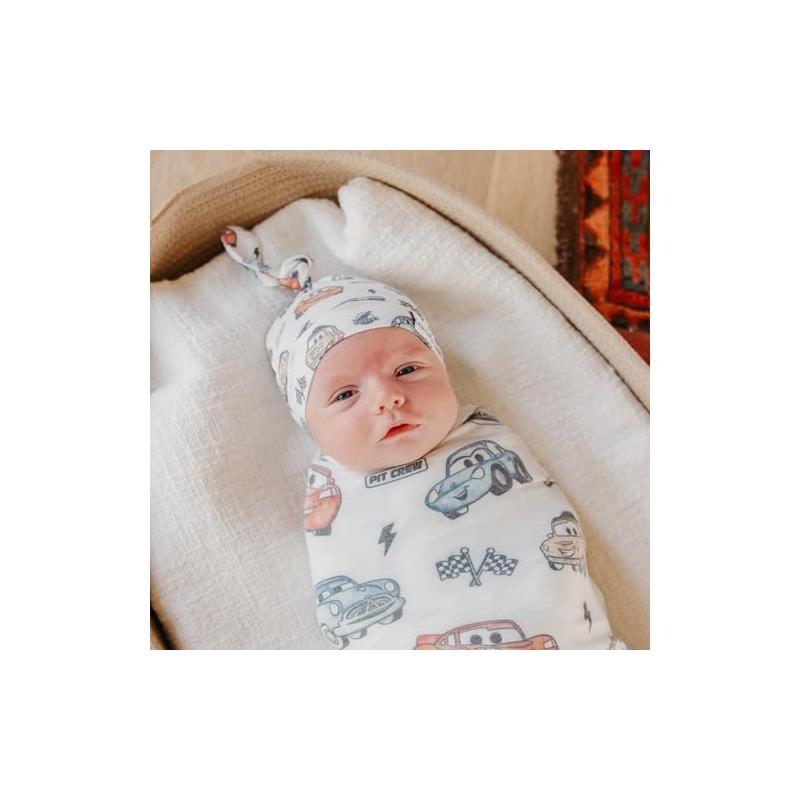 Baby wearing a Copper Pearl Disney Pixar Cars top knot hat and swaddle featuring colorful car designs.