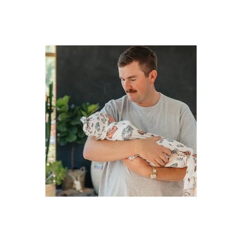 A father holding a wrapped baby in a Copper Pearl Disney Pixar Cars Top Knot Hat, showcasing playful car designs.