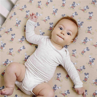Premium crib sheet featuring Mickey Mouse print with a baby in a light onesie lying on it.