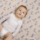 Baby lying on a beige crib sheet featuring a playful Mickey Mouse pattern, wearing a light long-sleeve onesie.