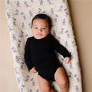 Baby lying on a Mickey Mouse-patterned diaper changing pad cover, wearing a black long-sleeve onesie.