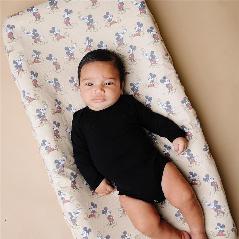 Infant lying on a Disney-themed diaper changing pad cover featuring Mickey Mouse, wearing a black long-sleeve onesie.