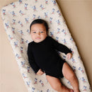 Infant lying on a Disney-themed diaper changing pad cover featuring Mickey Mouse, wearing a black long-sleeve onesie.