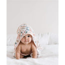 Hooded floral towel covering a baby, showcasing its soft fabric and design, on a bed with white bedding.
