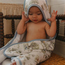 Hooded towel featuring a cute woodland print, wrapped around a toddler sitting on a wooden chair, with a smiling expression.