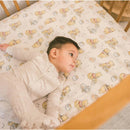 Premium crib sheet featuring a whimsical Winnie the Pooh design with a baby lying on it in a crib.