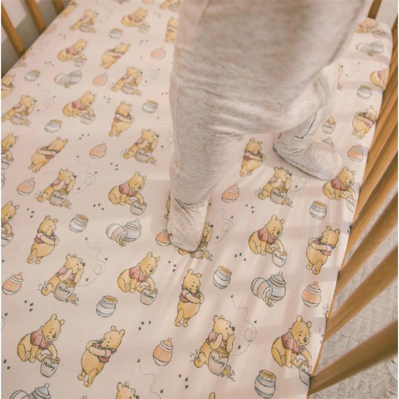 Premium crib sheet featuring a whimsical Winnie the Pooh design with honey pots, used in a crib with a toddler standing.