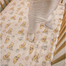 Premium crib sheet featuring a whimsical Winnie the Pooh design with honey pots, used in a crib with a toddler standing.