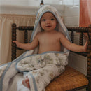 Baby seated on a wooden chair wearing a Copper Pearl Hunny premium knit hooded towel with whimsical floral patterns.