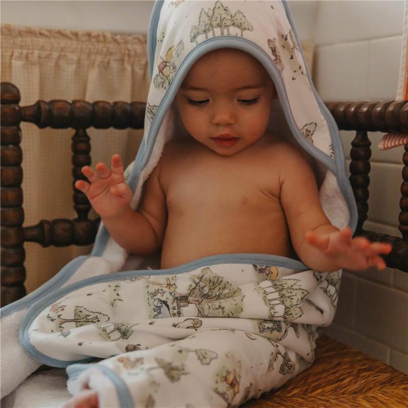 Hooded towel featuring playful forest designs, draped over a seated infant with a relaxed expression.
