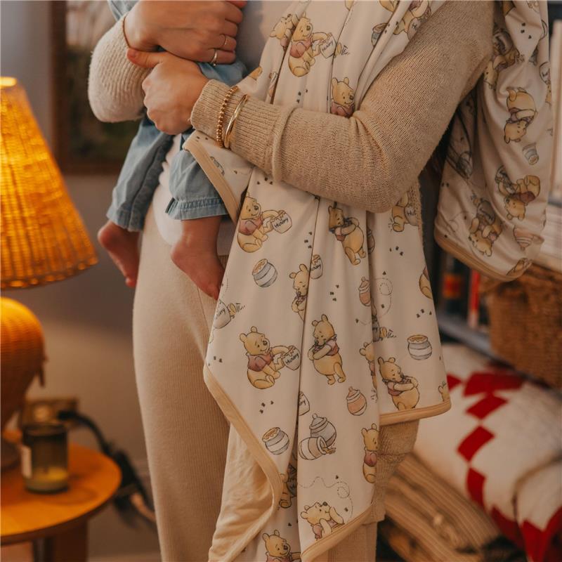 Large premium knit baby quilt blanket featuring a whimsical Winnie the Pooh design, held by a parent with a child.