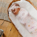 Large premium knit baby swaddle blanket featuring whimsical designs, with an infant asleep in a woven basket.