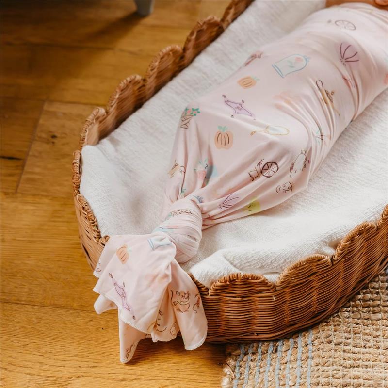 Large knit baby swaddle receiving blanket in pastel pink with whimsical illustrations, neatly wrapped in a wicker basket.