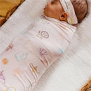 Large pink baby swaddle blanket with whimsical Enchanted Friends design, wrapped around a sleeping infant.