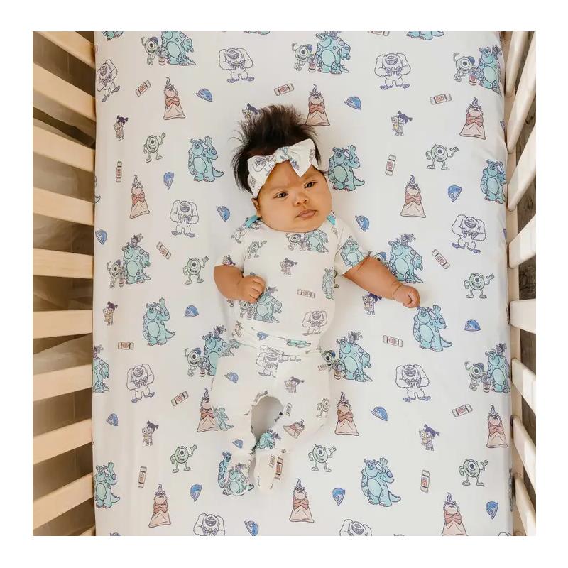 Premium crib sheet featuring Monsters Inc. characters, with a baby wearing a matching outfit and headband in a crib.