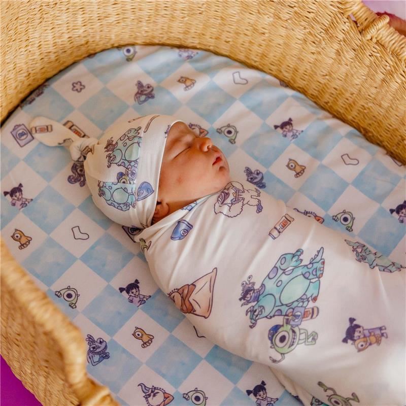 Top knot hat and swaddle featuring Monsters Inc characters, with a baby peacefully sleeping in a woven basket.