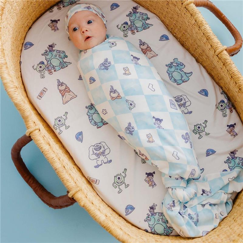Knit blanket featuring Monsters Inc characters, wrapped around a baby in a wicker basket with a patterned sheet.