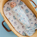 Knit blanket featuring Monsters Inc characters, wrapped around a baby in a wicker basket with a patterned sheet.